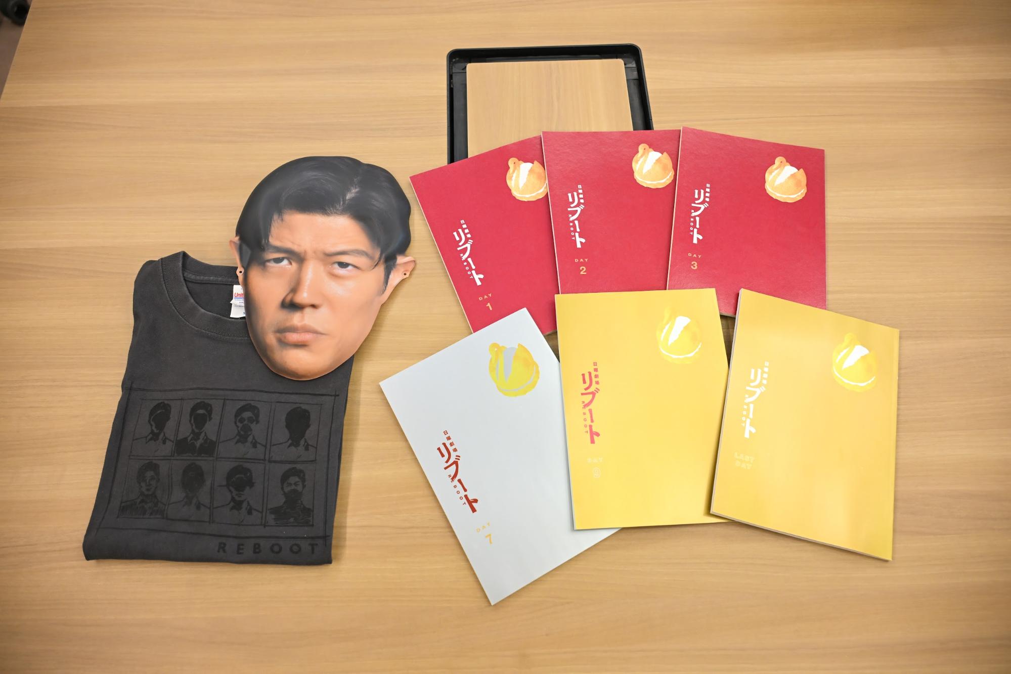 制作発表などで使用したお面、鈴木亮平さんがキャスト・スタッフにプレゼントしてくださったというTシャツ、台本には「ハヤセシュークリーム」の絵が